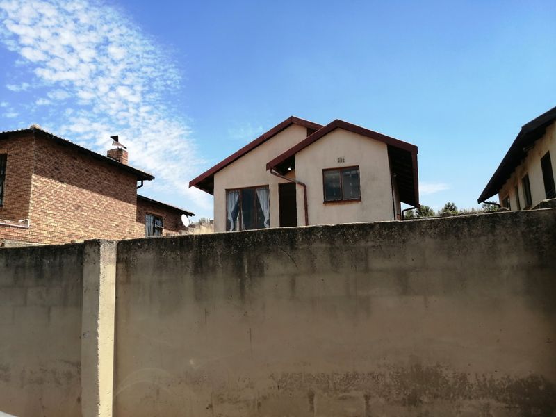 View of the rear elevation of the house featuring a pitched roof and a concrete boundary wall in the foreground.