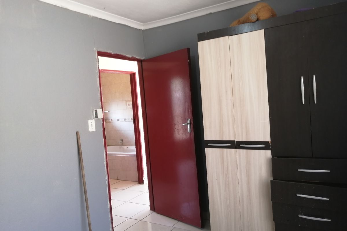 A bedroom featuring grey walls and tiled flooring, with an adjoining bathroom visible through the open doorway.