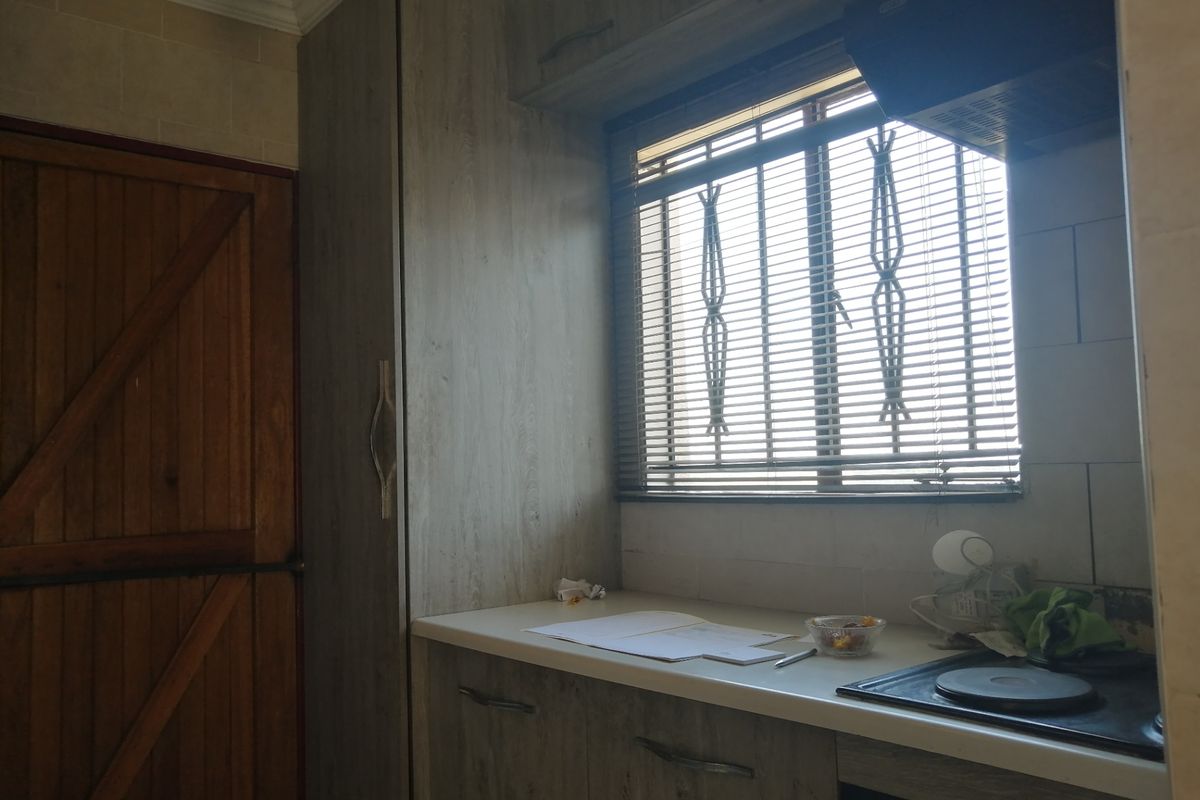 A functional kitchen area featuring wood-look cabinetry, a built-in electric hob with extractor fan, and a window with security bars.