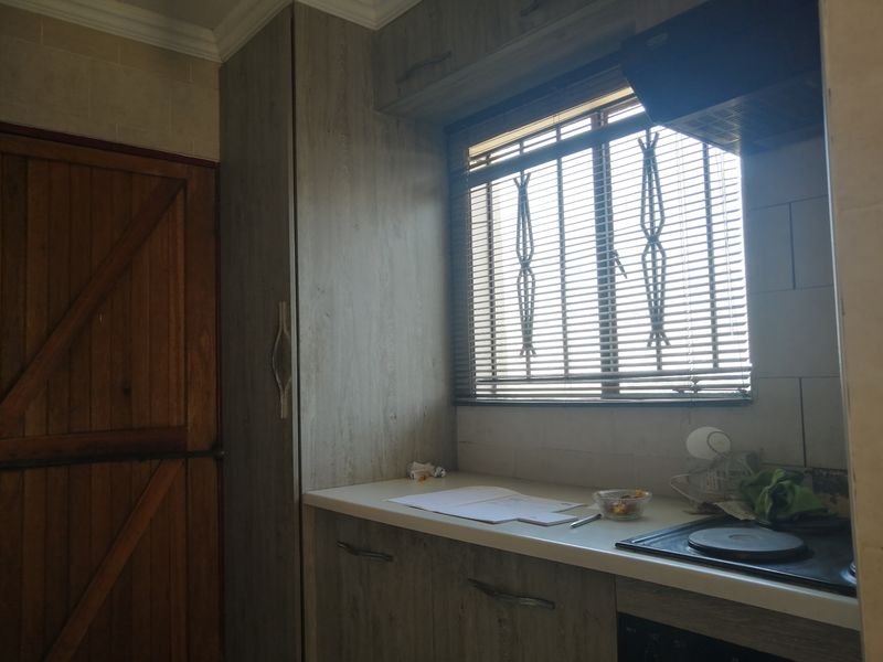 A functional kitchen area featuring wood-look cabinetry, a built-in electric hob with extractor fan, and a window with security bars.