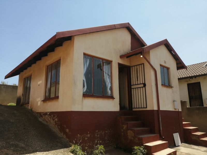 Front elevation of a detached house featuring a pitched roof, metal security gate, and concrete entrance stairs, showing signs of exterior wear.