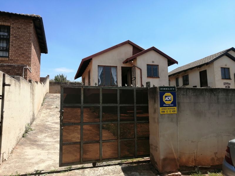 Front view of a detached house featuring a metal driveway gate, perimeter wall, and concrete driveway access.