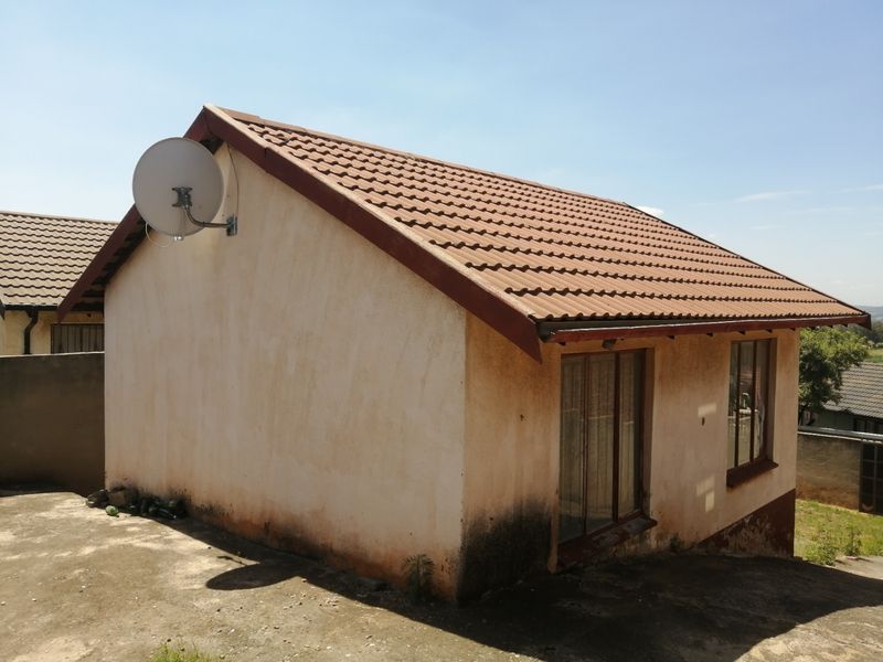 Rear view of a detached house featuring a tiled roof, satellite dish, and visible exterior wall staining requiring maintenance.