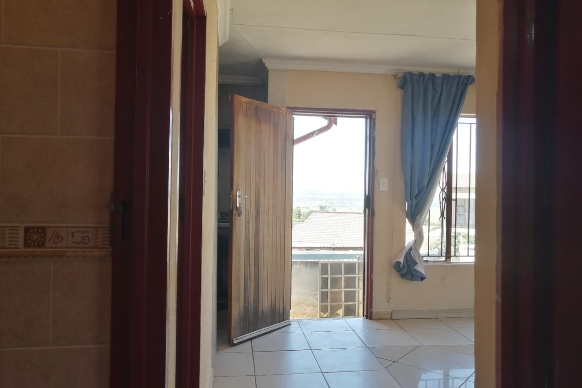An empty living area featuring tiled flooring, security bars on windows, and a timber door leading to an outdoor space.
