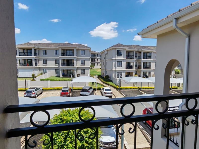 View from a balcony overlooking the apartment complex grounds, featuring paved parking areas with shade ports and surrounding residential buildings.