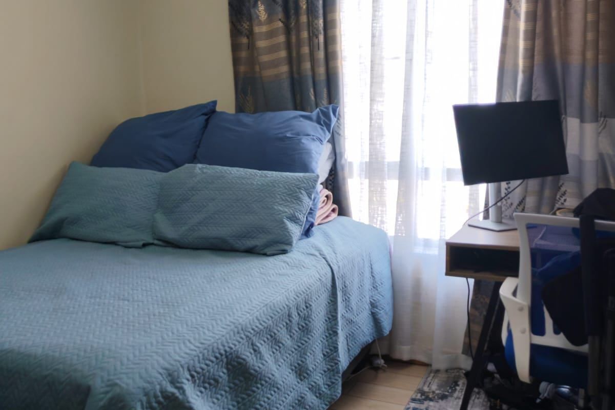 A compact bedroom featuring light-toned wood-look flooring and a window with curtains, providing a functional space for rest and study.