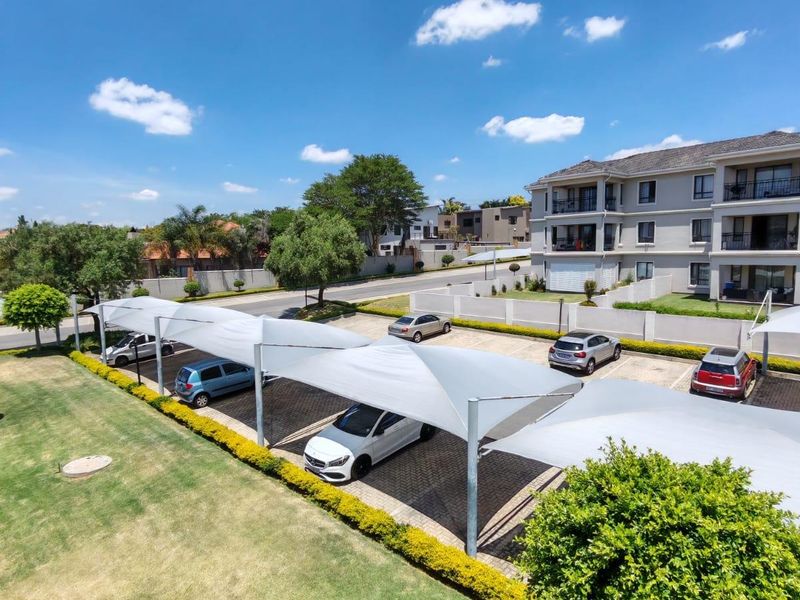 An elevated view of the apartment complex parking area featuring covered shade-cloth carports and landscaped garden surrounds.
