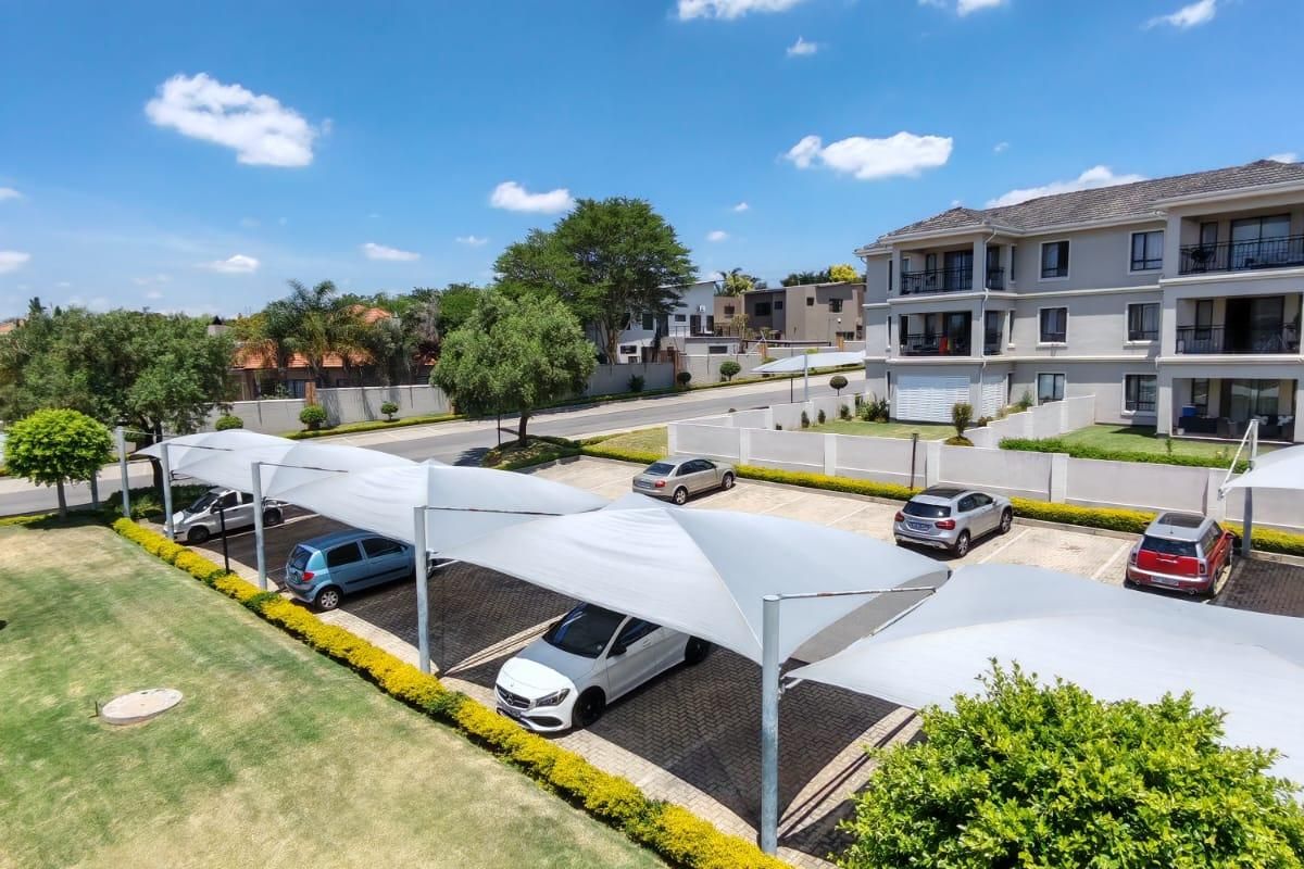 An elevated view of the apartment complex parking area featuring covered shade-cloth carports and landscaped garden surrounds.