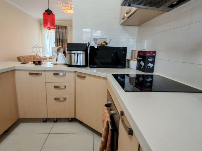 A functional kitchen featuring light wood cabinetry, a built-in oven, a glass cooktop, and a stainless steel extractor fan with tiled splashbacks.