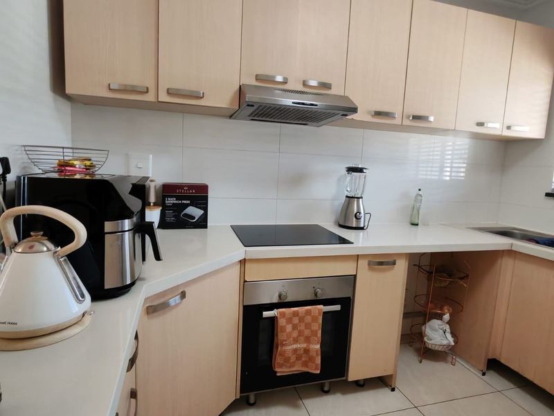 Functional kitchen featuring light wood cabinetry, white countertops, integrated oven, electric hob, and stainless steel extractor fan.