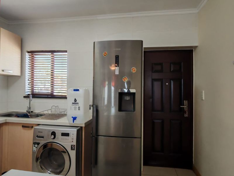 A functional kitchen area featuring light wood cabinetry, a stainless steel sink, and space for a washing machine and refrigerator.