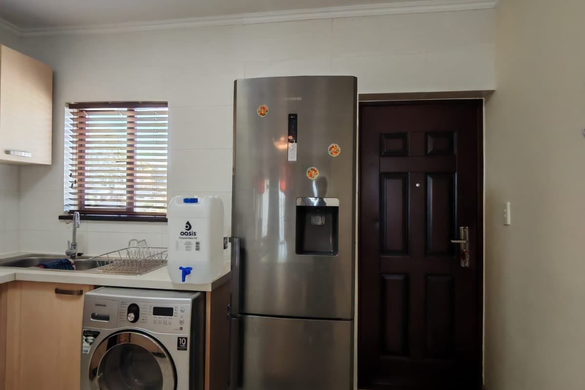 A functional kitchen area featuring light wood cabinetry, a stainless steel sink, and space for a washing machine and refrigerator.