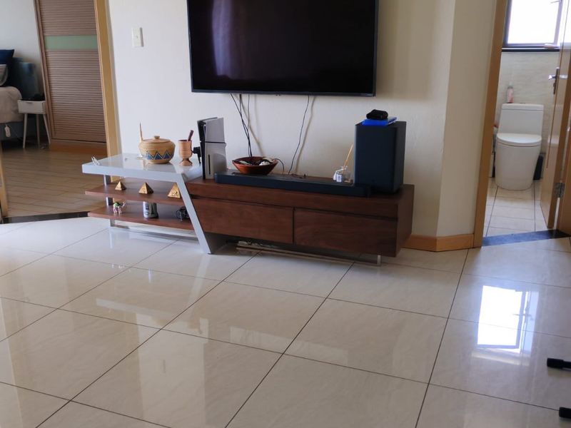 A living area featuring polished porcelain floor tiles, neutral wall finishes, and access to adjacent bedroom and bathroom spaces.