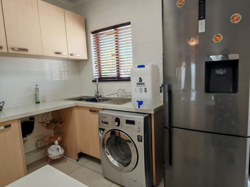 Compact kitchen featuring light wood cabinetry, tiled splashback, integrated sink, and space for a washing machine.