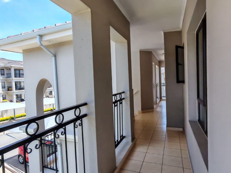 A covered balcony featuring tiled flooring and decorative wrought iron railings, offering an elevated view of the apartment complex grounds.