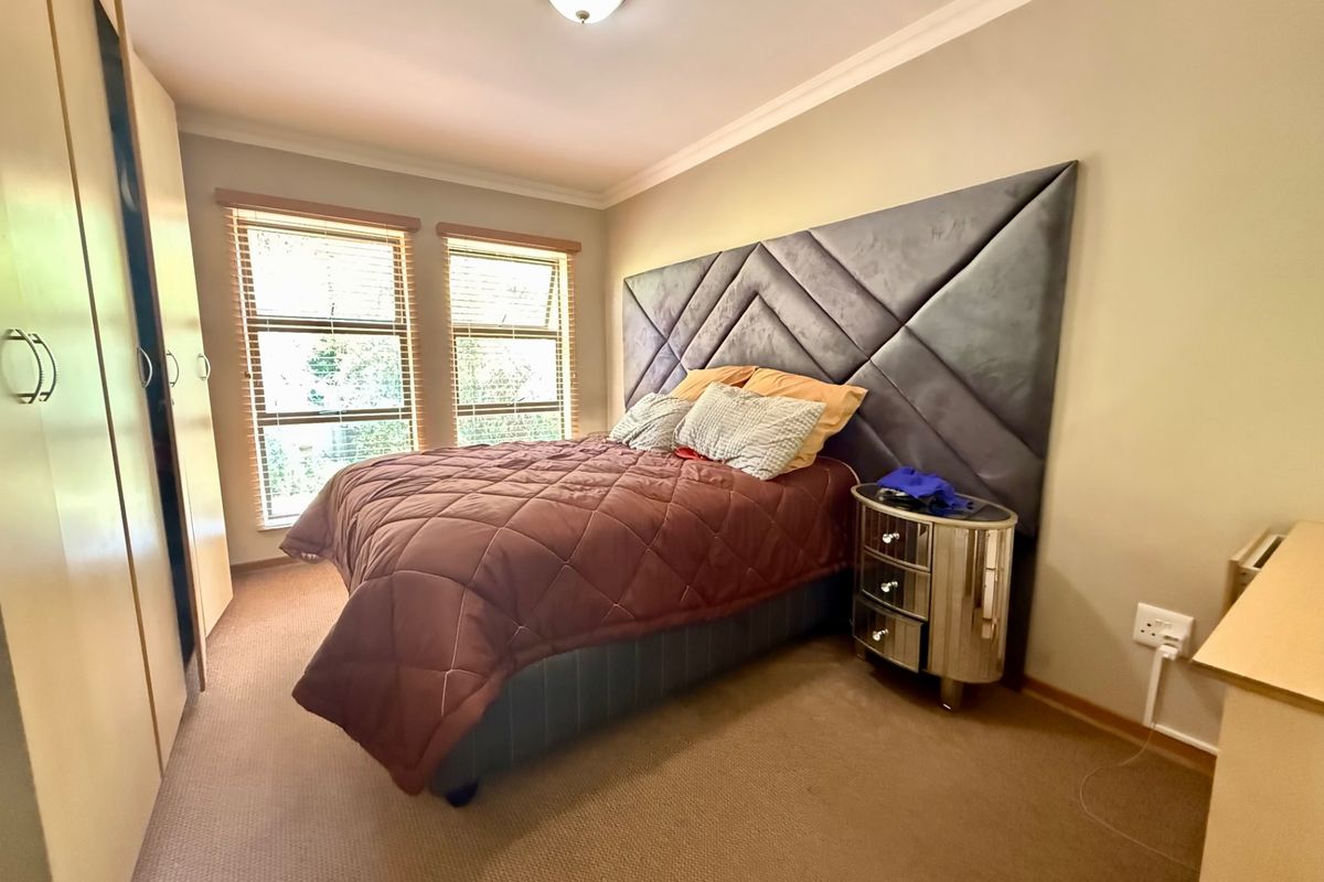 A well-maintained bedroom featuring built-in cupboards, carpeted flooring, and large windows with venetian blinds, providing a comfortable and functional living space.