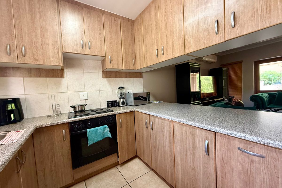 Functional kitchen featuring wood-look laminate cabinetry, granite-style countertops, built-in oven, electric hob, and a convenient breakfast bar overlooking the living area.