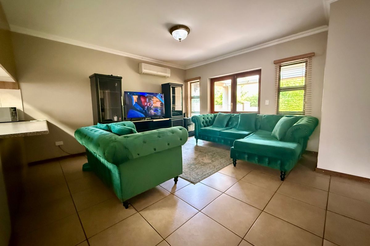 A spacious living room featuring tiled flooring, a wall-mounted air conditioning unit, and direct access to the patio through wooden french doors.