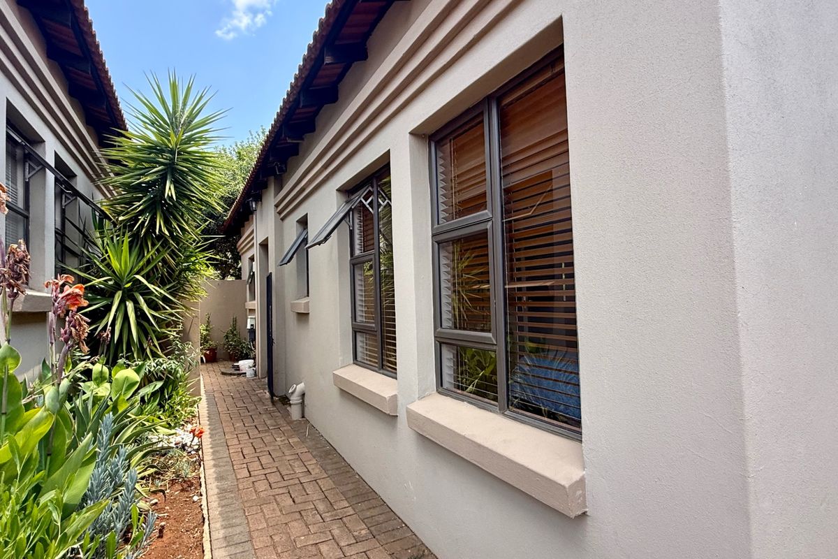 A side exterior view of the townhouse featuring a brick paved walkway, well-maintained plastered walls, and modern aluminium window frames.