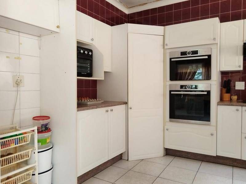A dated kitchen featuring white cabinetry, built-in double ovens, tiled backsplash, and tiled flooring, currently showing signs of wear and ceiling damage.
