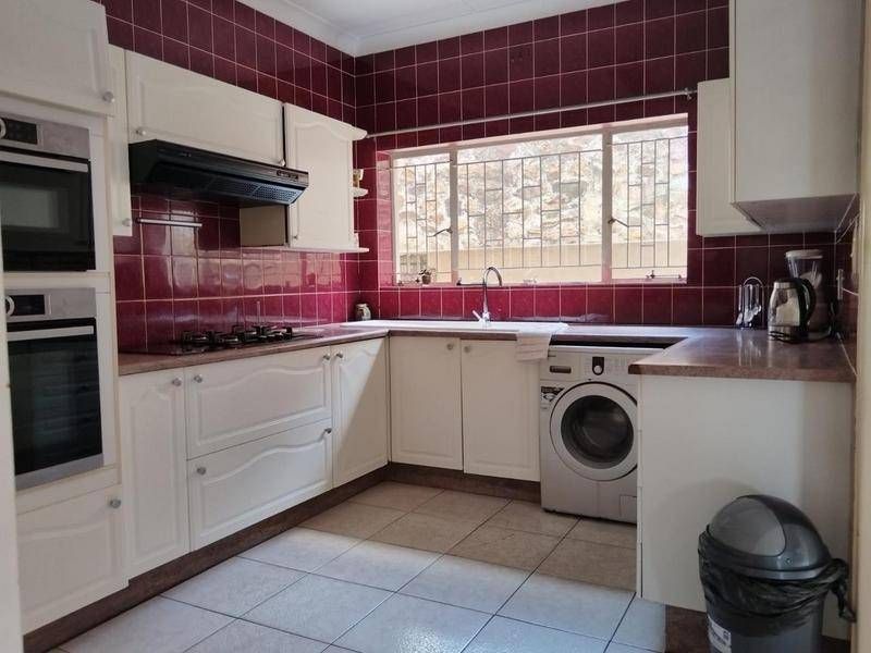 A functional kitchen featuring built-in oven, gas hob, extractor fan, and ample cabinetry with a tiled splashback and integrated laundry space.