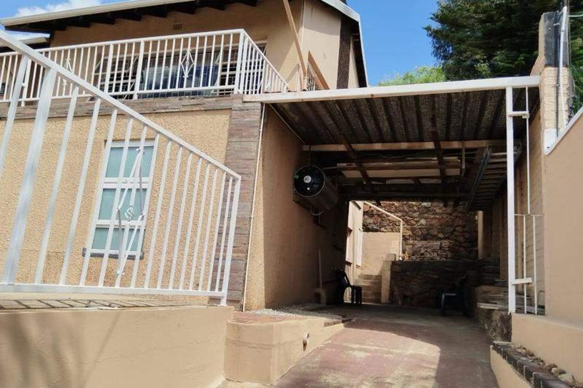 Rear exterior view featuring a paved driveway, covered carport area, and an elevated balcony with metal railings.