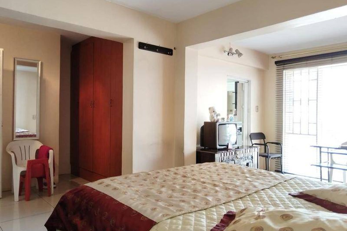 A functional bedroom featuring built-in wardrobe storage, tiled flooring, and access to a balcony through a secure sliding door.