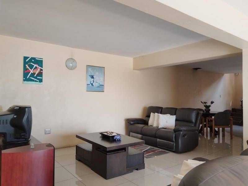 Spacious open-plan living area featuring neutral tiled flooring and a structural ceiling beam, offering a versatile layout for lounge and dining arrangements.