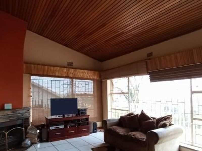 Spacious living room featuring a stone fireplace, high timber-clad vaulted ceilings, and large windows providing ample natural light.