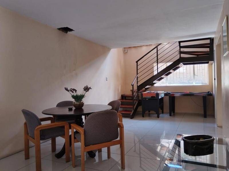 Open plan living area featuring tiled flooring and a metal staircase, with visible ceiling damage requiring repair.