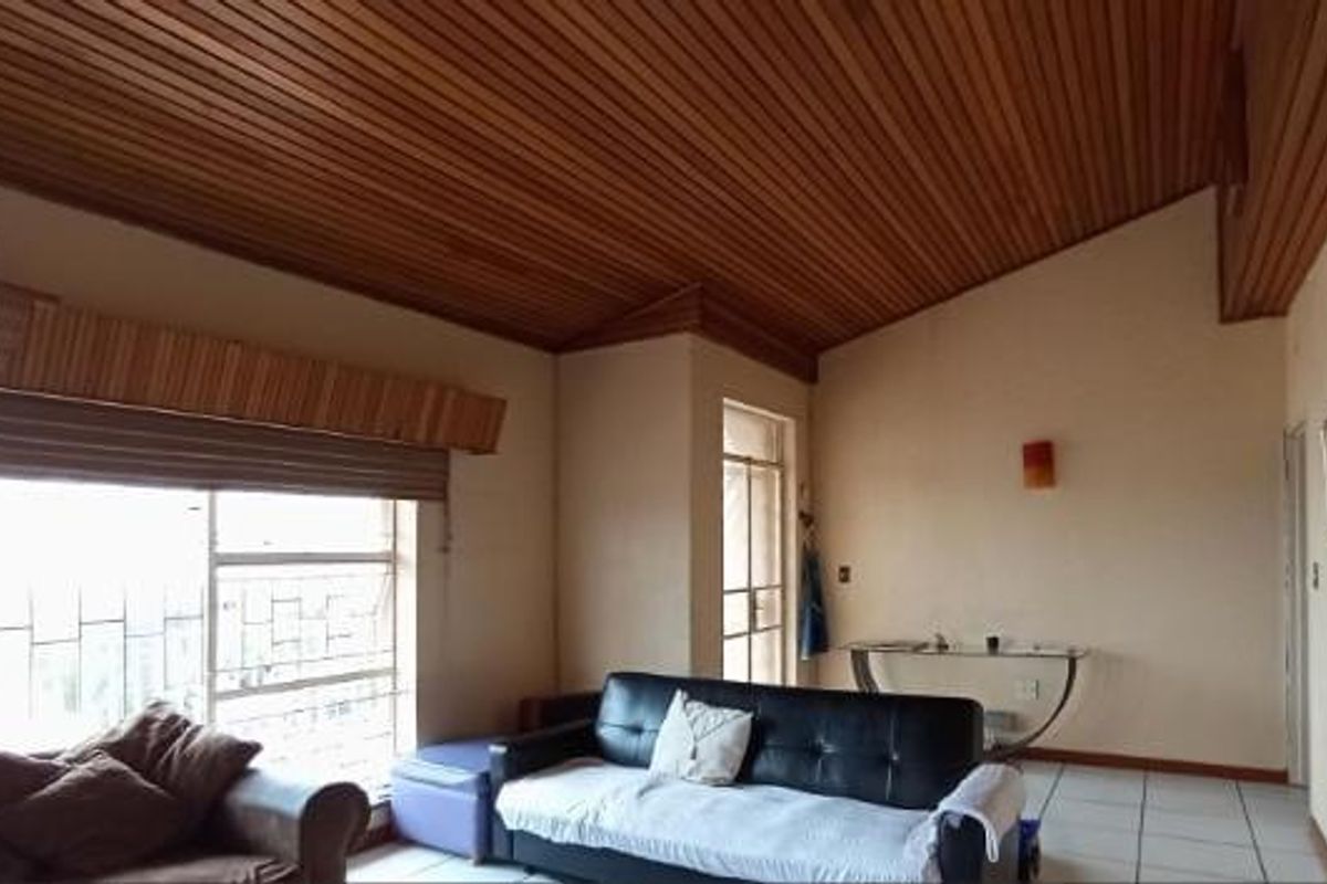 Spacious living area featuring a distinctive timber-clad raked ceiling, tiled flooring, and large windows with security bars.