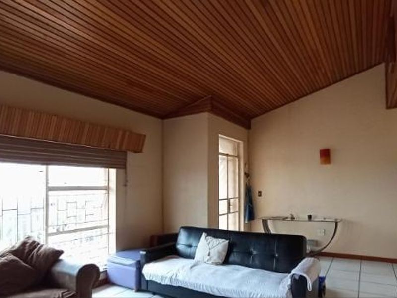 Spacious living area featuring a distinctive timber-clad raked ceiling, tiled flooring, and large windows with security bars.