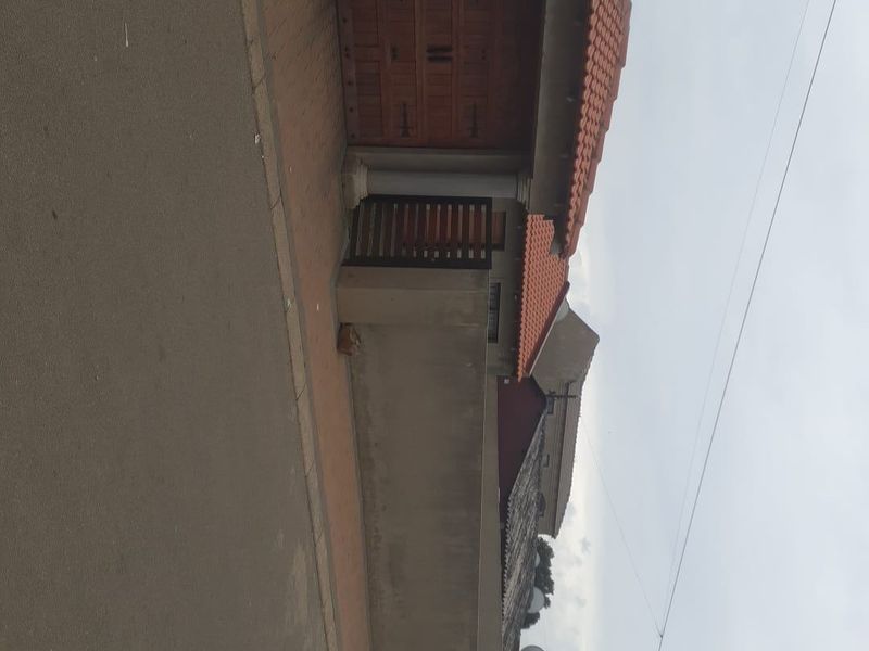 Front exterior view of the property featuring a tiled roof, wooden garage door, and a paved driveway with a boundary wall.