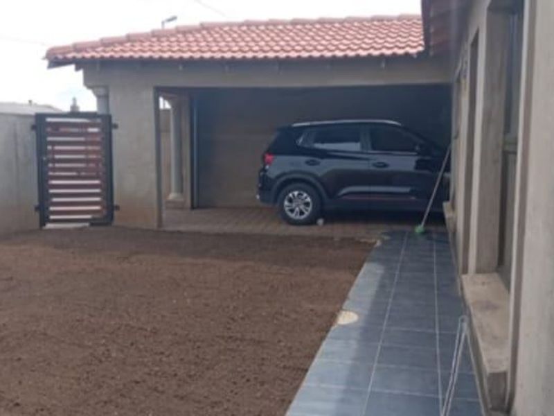 Rear exterior view showing a covered patio area, paved driveway, and boundary wall with an unfinished garden space.