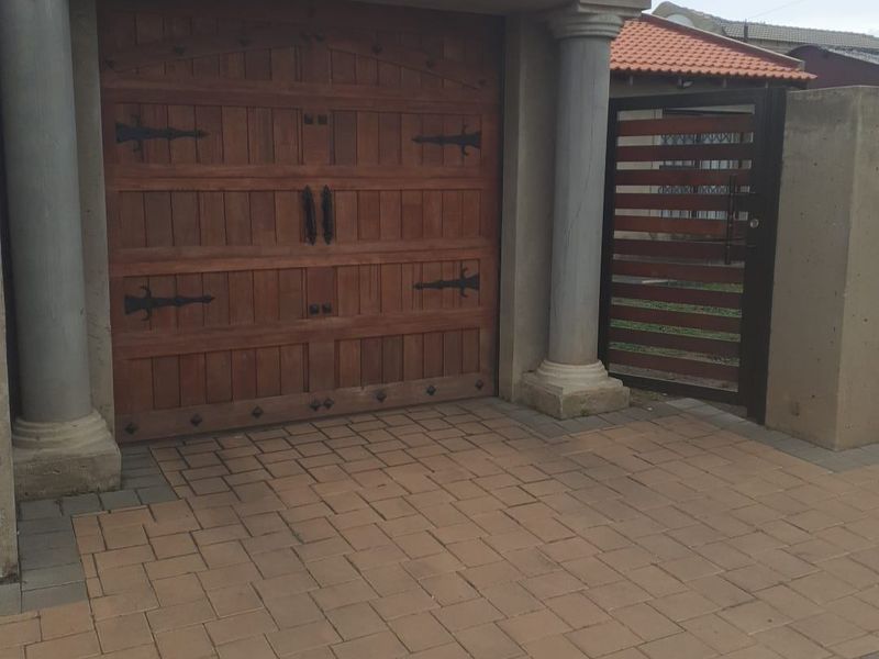 A secure garage entrance featuring a rustic wooden door, decorative columns, and a paved driveway with an adjacent pedestrian gate.
