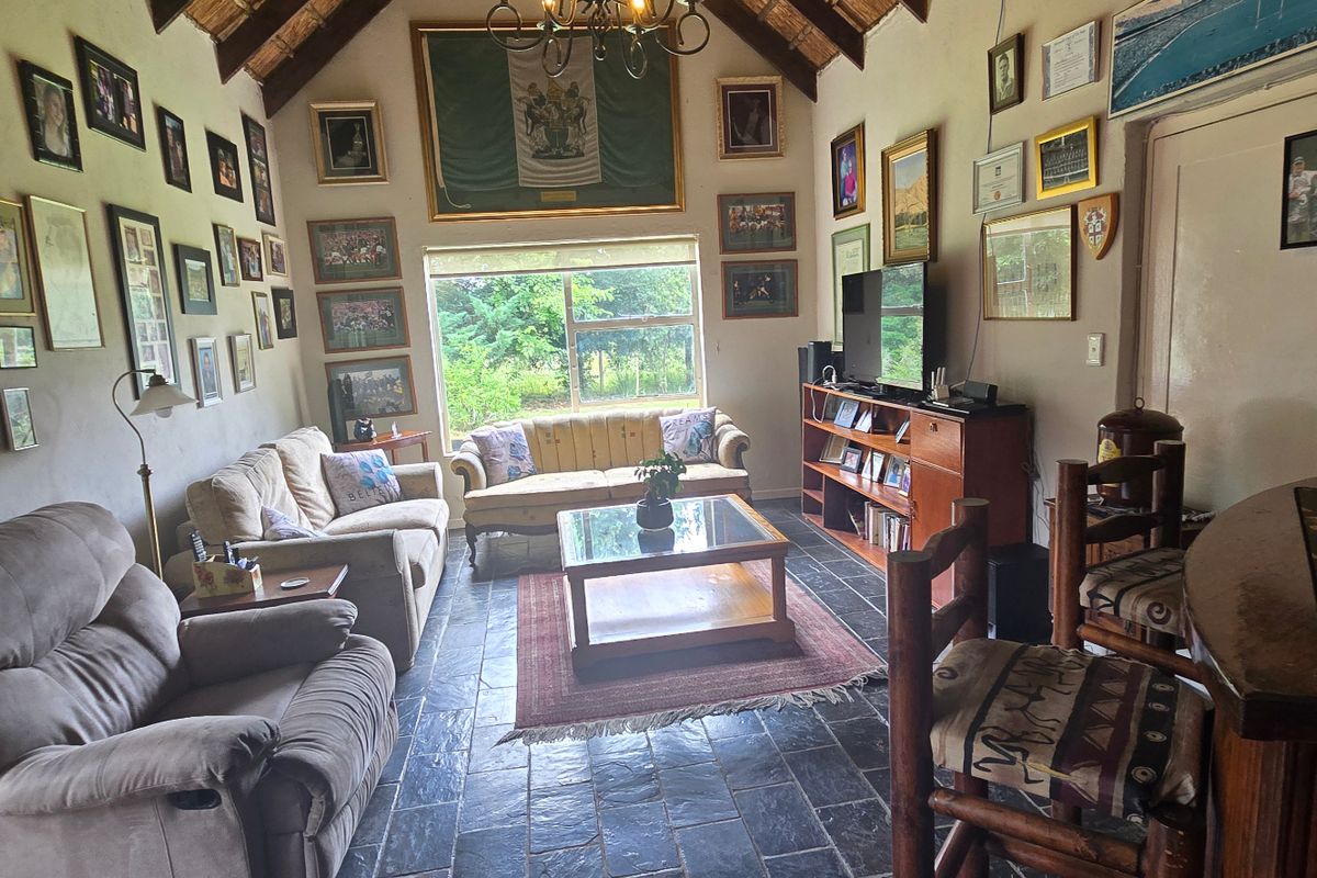 A rustic living room featuring a high vaulted thatched ceiling with exposed rafters, slate flooring, and a built-in bar area.