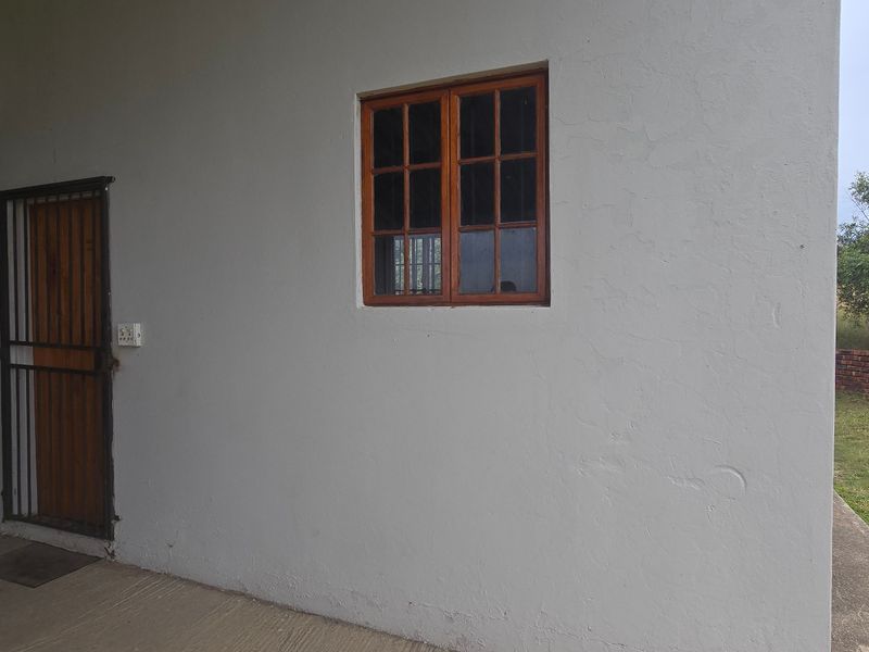 A view of the rear exterior wall featuring a timber-framed window, security gate, and concrete patio area on the farm property.