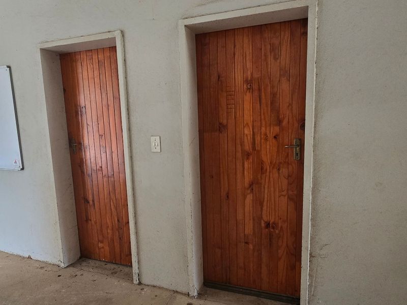A utilitarian hallway featuring two wooden doors and concrete flooring, showing signs of wear on the wall surfaces.