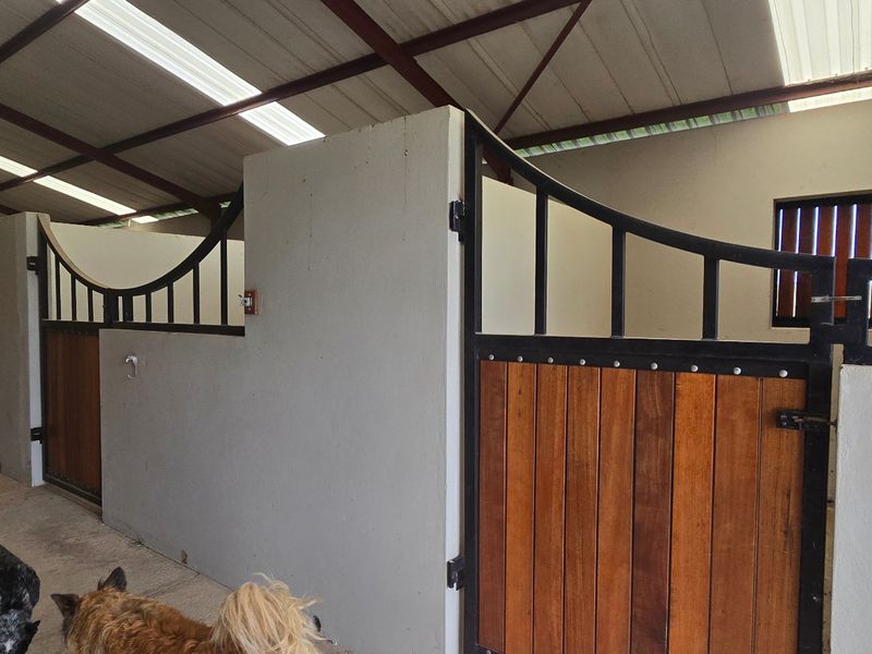 A well-maintained stable block featuring individual stalls with timber and metal doors, concrete flooring, and an open-truss roof structure with natural lighting.