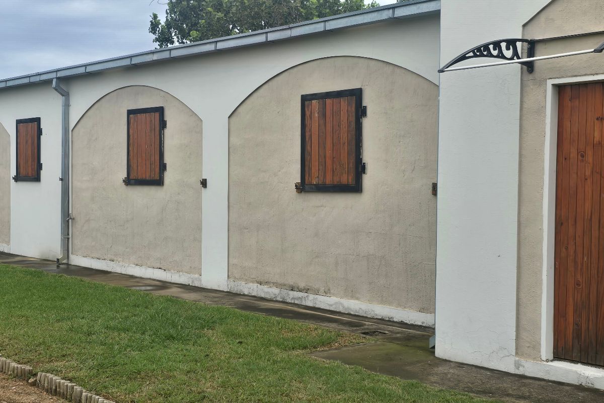 Exterior view of a farm building featuring arched wall detailing, timber shutters, and a covered entrance.