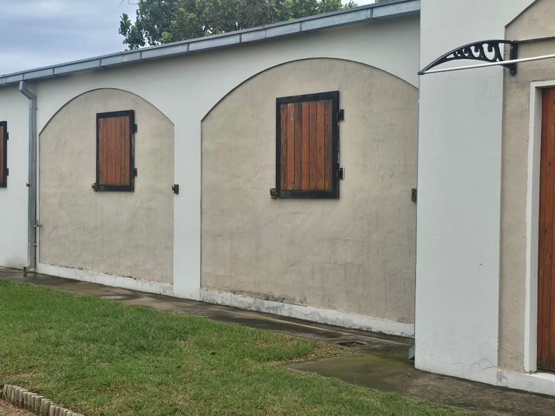 Exterior view of a farm building featuring arched wall detailing, timber shutters, and a covered entrance.