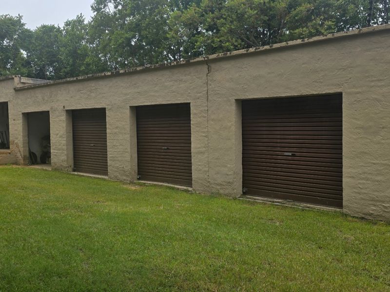A long exterior view of a multi-bay garage block featuring several roller shutter doors and a side access door on a rural farm property.