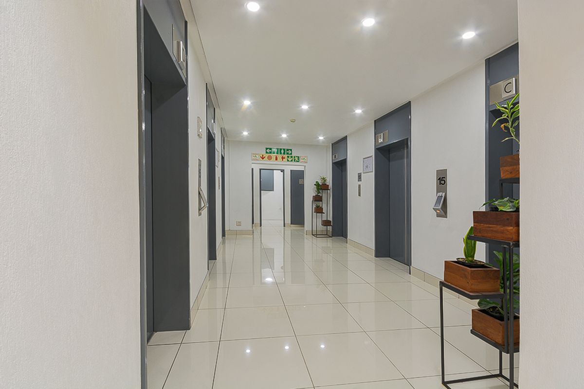 A clean, modern commercial hallway featuring polished tile flooring, recessed ceiling lighting, and multiple elevator access points.