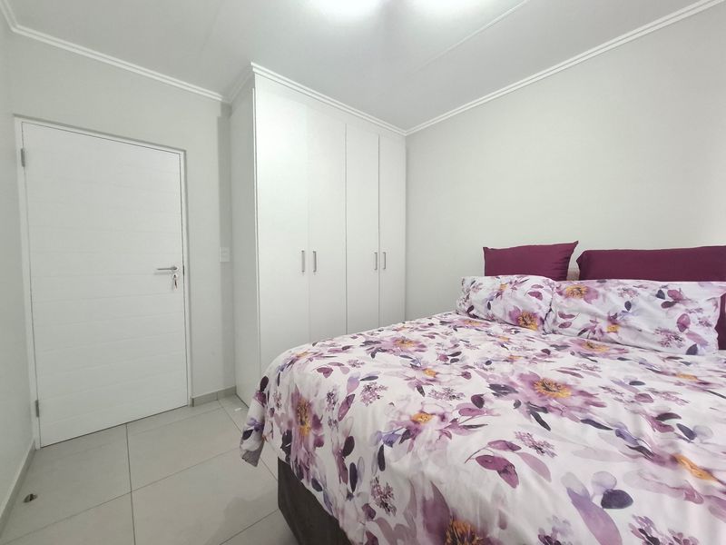 A clean and well-maintained bedroom featuring neutral tiled flooring, white built-in wardrobes, and simple cornice detailing.