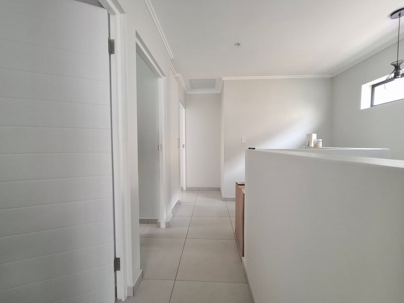 A bright and neutral hallway featuring tiled flooring, clean white walls, and modern recessed lighting, providing access to multiple rooms.