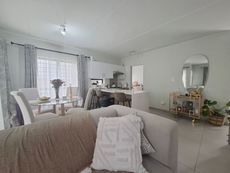 An open-plan living and dining area featuring a modern kitchen with a breakfast island, tiled floors, and direct access to the outdoors.