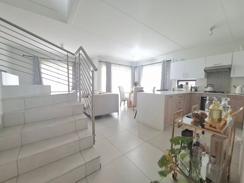 Modern open-plan living area featuring a tiled staircase with stainless steel balustrade, integrated kitchen cabinetry, and a functional kitchen island.
