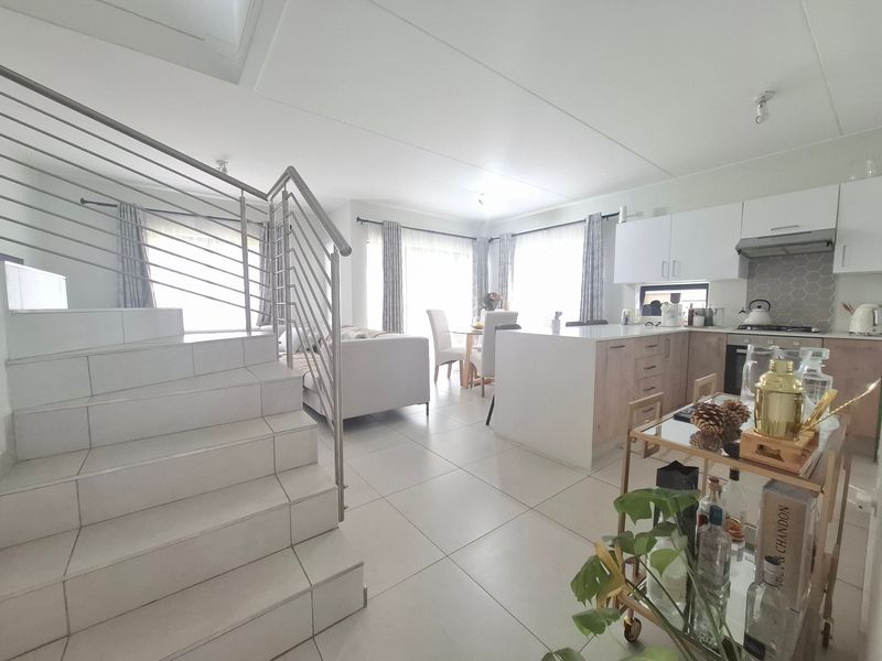 Spacious open-plan living area featuring a modern kitchen with island, tiled flooring, and a contemporary staircase with stainless steel balustrade.