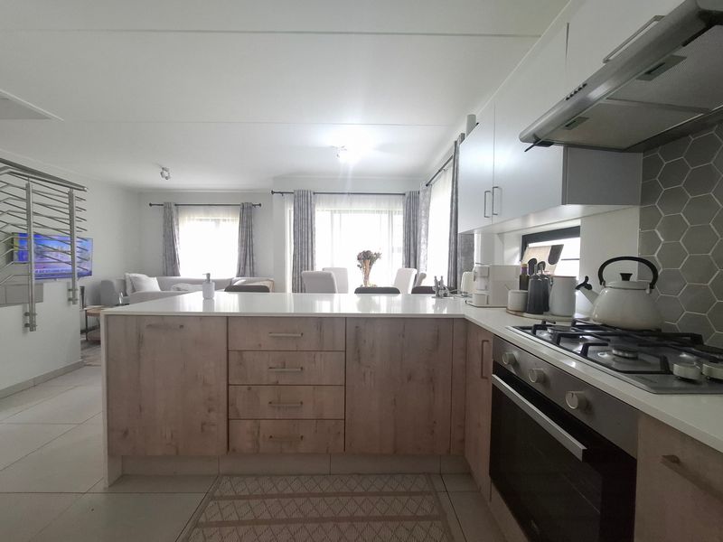 Modern open-plan kitchen featuring a central island, gas hob, extractor fan, and stylish hexagonal backsplash, seamlessly flowing into the adjacent living and dining area.