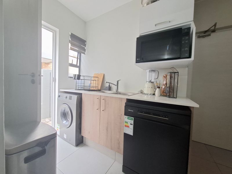 A functional laundry area featuring built-in cabinetry, a stainless steel sink, and integrated microwave space with direct access to an outdoor area.